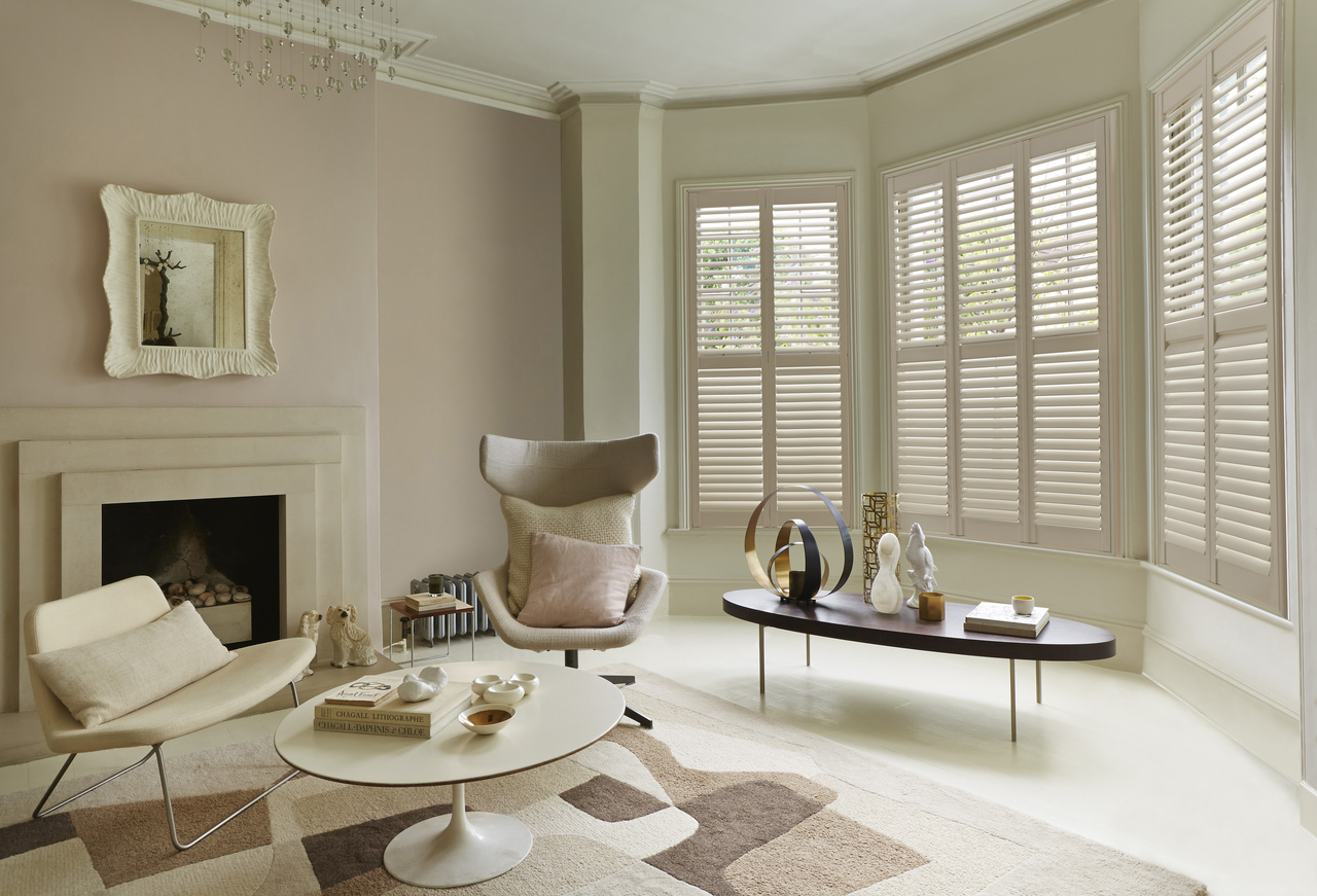 Neutral lounge with rug in colour blocks of browns and creams and curved bay windows dressed in creamy-light beige shutters.