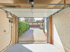 Interior of an empty garage with the door open, looking out onto the driveway.