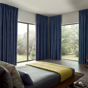 Dark blue curtains fitted to two wide windows in a bedroom with dark wooden floors and a grey bed 