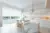 Open-plan white kitchen with trio of window and doors dressed in white roller blind with marble island with white chairs and modern pendant light.