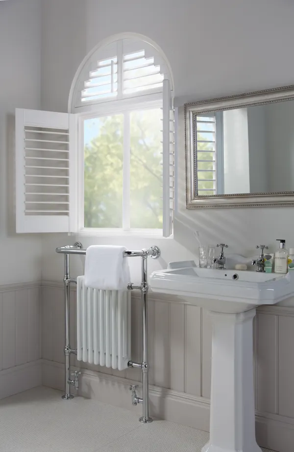 white shutters fully open in a bathroom window letting light in, with arched top of the shutters closed with slats open