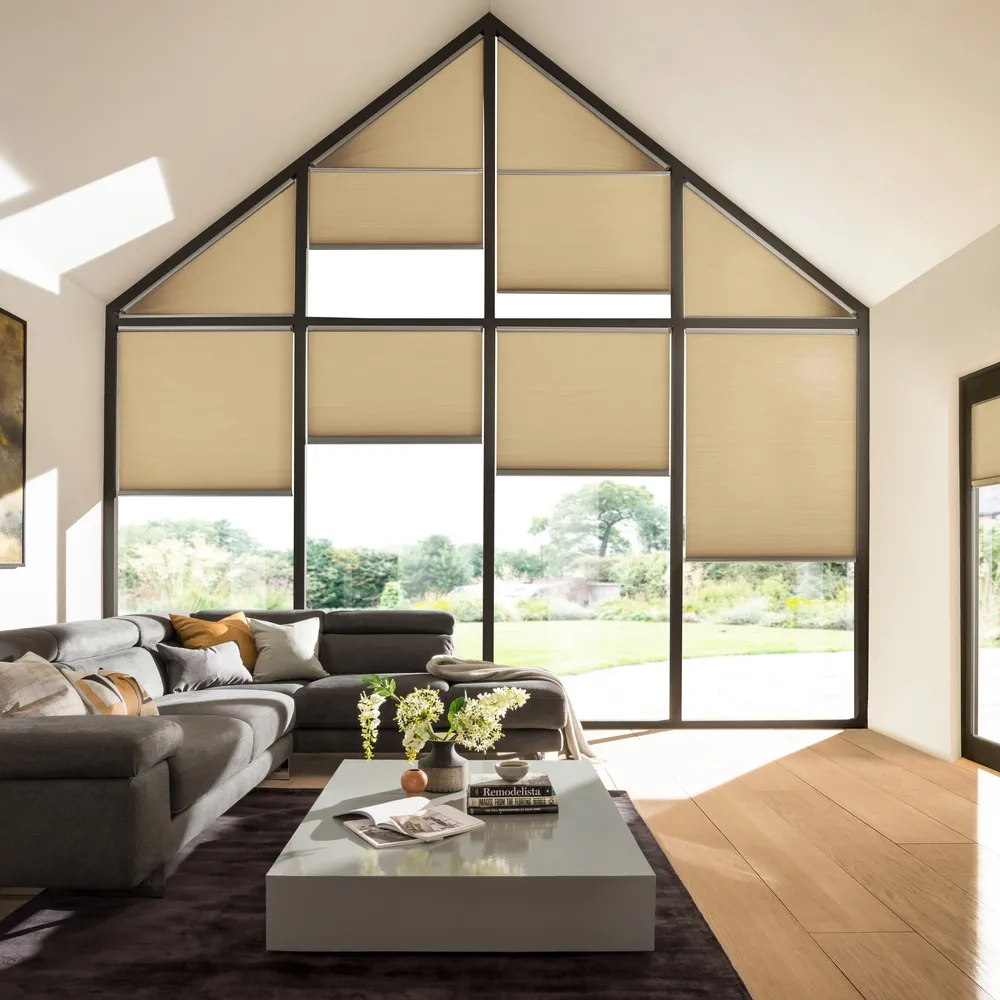 Gable end windows and doors in living room with buttermilk walls, brown sofa, grey low table, wood floor, French doors on right hand wall, all windows and doors dressed in pale caramel Duette blinds at varying heights.