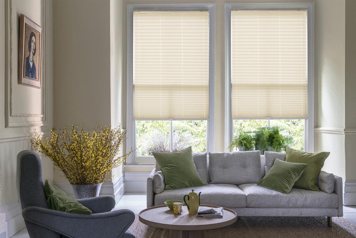 natural Allegro Biscotti Pleated blind are fitted to a series of windows in a kitchen decorated with marble counter tops, white walls and drawers. The Pleated blinds are decorated in a geometric style.