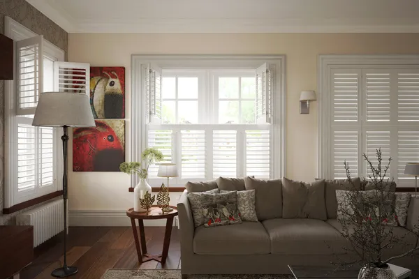 Corner of living room with three sets of windows dressed in white tier on tier shutters, left and central windows top section open, bottom closed with louvres open, right and both closed with louvres slightly tilted, cream walls, abstract art on wall.