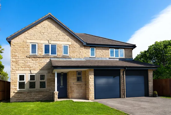 Yellow Cotswold stone-style house with integral  garage with two blue steel garage doors that match the front door.