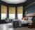 Large bedroom with wooden floor, bay window with three ochre faux velvet Roman blinds, navy walls, bed with white bedding and grey quilted throw,. 
