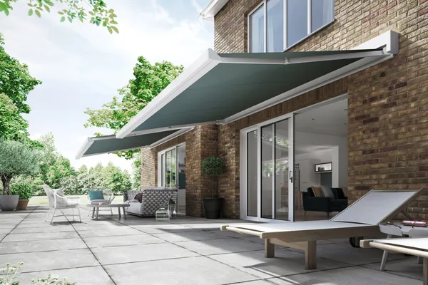 Side shot of house with two steel blue awnings extended over patio with furniture underneath.