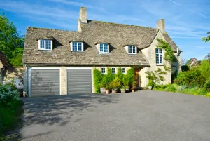Old-style stone house, with 8 forward facing windows, planters, a solid oak door, and light beige roller doors.