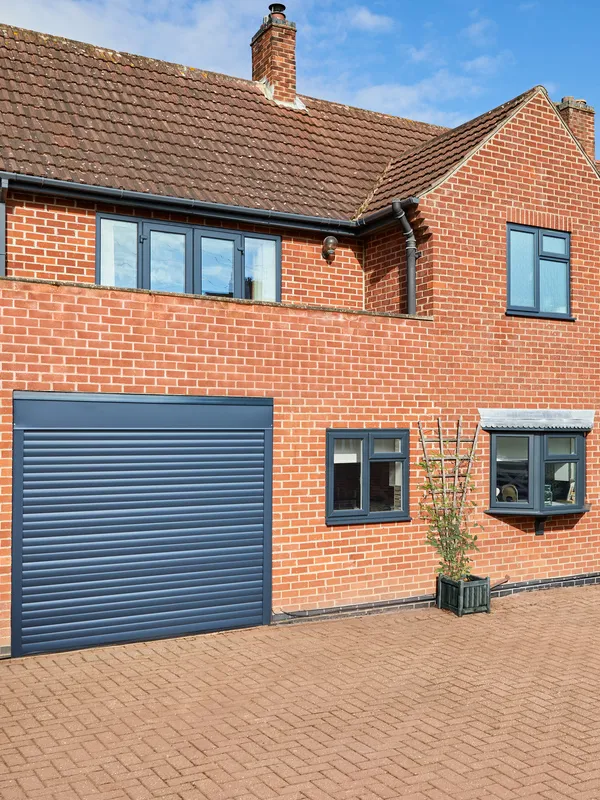 An orange brick house with a balcony, anthracite grey window frames and an anthracite grey roller garage door.