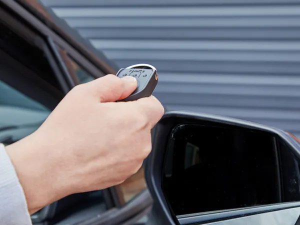 Hand coming out a car window holding a remote control fob which is pointing at the closed garage door ahead.) 