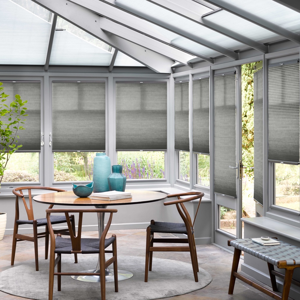 mid grey duette blinds three quarters lowered in conservatory with circular wooden table and chairs on a grey rug.