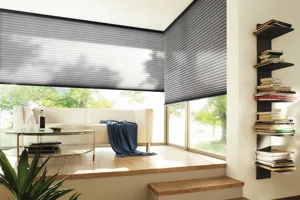 Raised seating area in wood with white modern couch and glass oval coffee table, smoky blue throw on couch and wall to wall window behind and to right dressed in smoky blue Duette blinds.