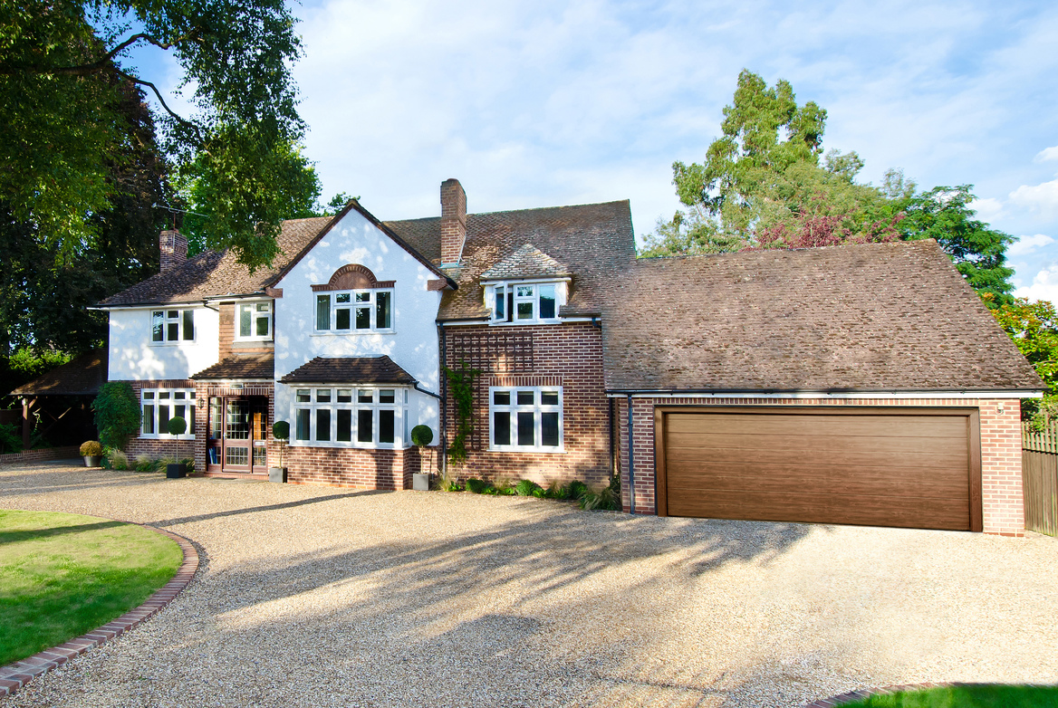 A large detached property with a garage attached with a brown sectional garage door and a shingle driveway.